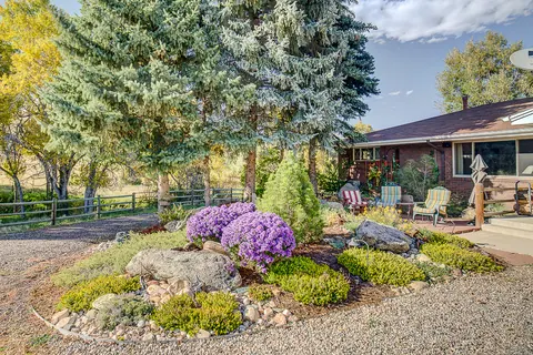 Boulder rockery with purple asters and golden groundcover beside a gravel drive and ranch-style home.