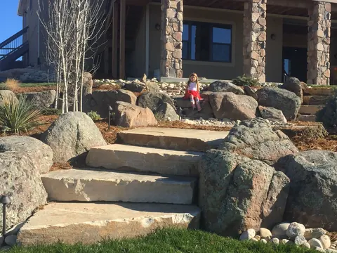 Wide sandstone steps flanked by large boulders and aspens leading to a porch in Fort Collins.