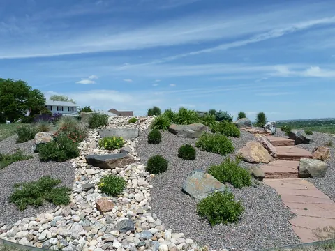 Dry creek of river rock and boulders with flagstone steps and shrubs on a gravel slope.