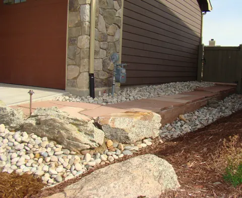 Flagstone slab and boulders set into river rock beside a home with a low-voltage path light.