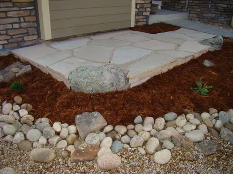 Flagstone landing with a boulder at a doorway edged by mulch and river rock.