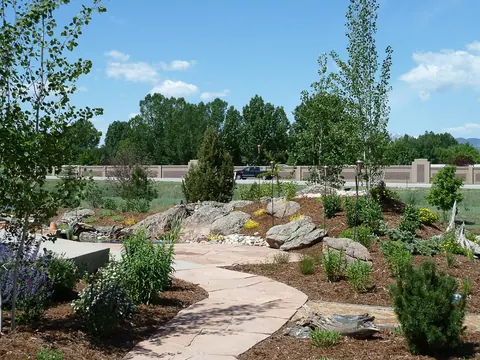 Curving flagstone path through boulders, perennials and young trees toward a flagstone patio.