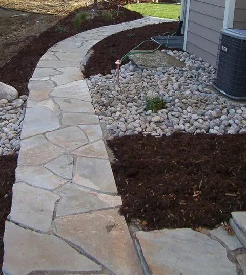 Flagstone path beside river rock and mulch along the side of a home.