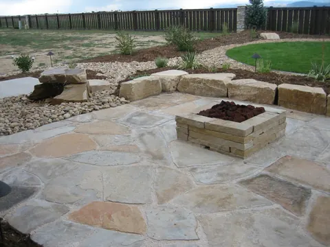 Large flagstone patio with a square fire pit and sandstone boulder bench wall.