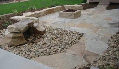 Flagstone patio with a square stone fire pit, river rock inlay and boulder seat wall.