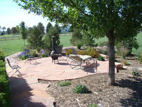 Round red flagstone patio under a shade tree with lounge chairs and a chiminea.