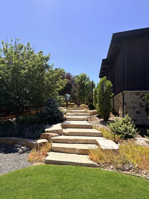 Wide natural stone slab steps climb a landscaped slope beside a lawn in Fort Collins.