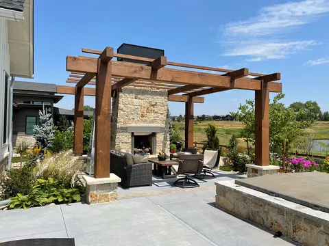 Concrete patio with a timber pergola, stone fireplace and outdoor seating overlooking open space in Timnath.
