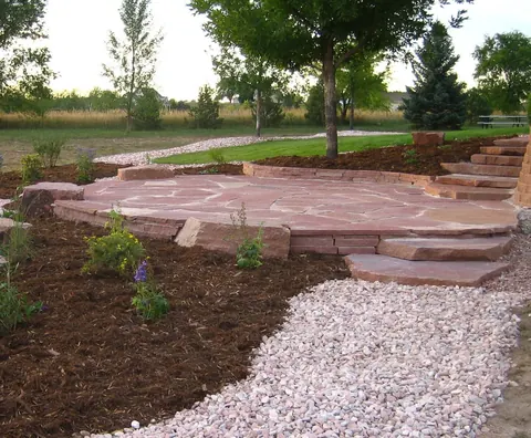 Raised red flagstone patio with steps, mulch beds and a pink gravel path.