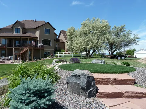 Red flagstone steps beside a round lawn, dark boulder and blue spruce in a gravel bed.