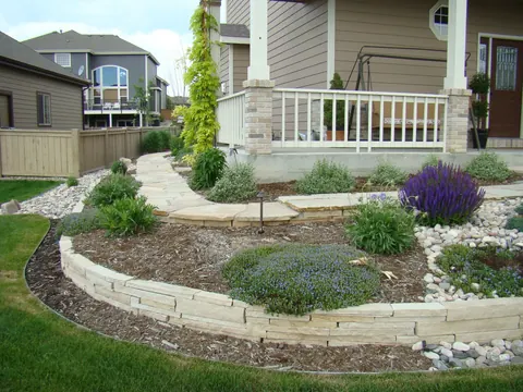 Layered stone edging around a raised bed with salvia and perennials in front of a porch.