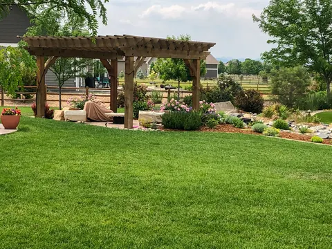 Timber pergola and patio seating area set behind a green lawn with rock and perennial beds.