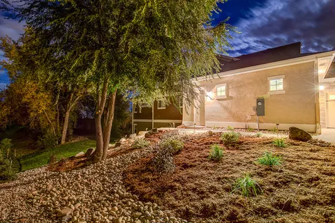 Evening landscape lighting washing over a river rock and mulch front bed beside a stucco home.