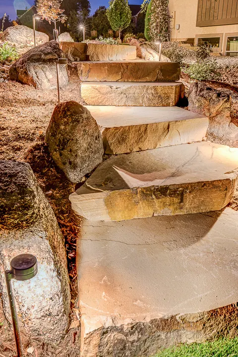 Sandstone slab steps and boulders lit by low-voltage landscape lighting at dusk.
