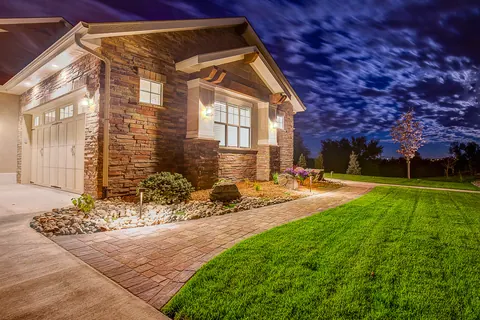 Landscape lighting at twilight on a stone-accented home with a paver walkway and lawn.