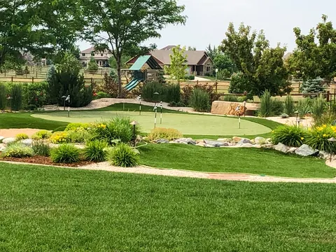 Backyard putting green framed by boulders, ornamental grasses and flowering perennials.