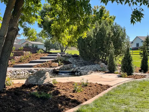 Backyard dry stream with a small waterfall, boulders and flagstone path under shade trees in Timnath.