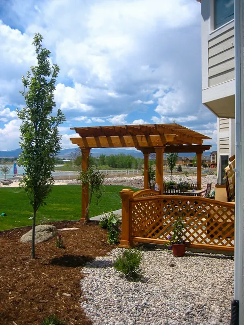 Cedar pergola with lattice, a gravel path and a young tree beside a new home.