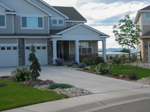 Driveway front yard with an evergreen, river rock edging and low plantings beside a lawn.