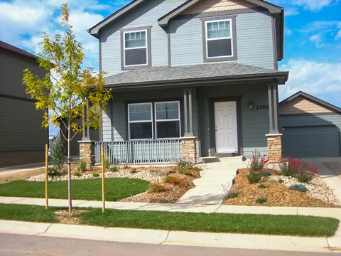 Front walkway with mulch and gravel perennial beds, grasses and young trees at a blue-gray home.