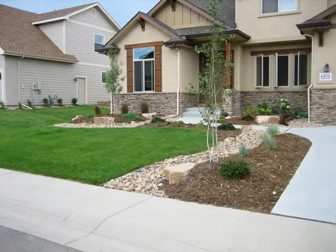 Front yard river rock dry creek, flagstone slab and mulch bed curving beside a lawn.