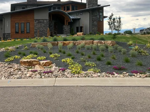 Terraced gravel front yard bed with flat boulders, yellow flowers and grasses by a contemporary home.