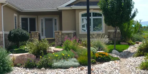 Front yard bed of grasses and perennials with a river rock dry path.