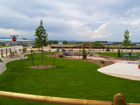 Wide lawn with young trees, a curved concrete patio and a rail fence.