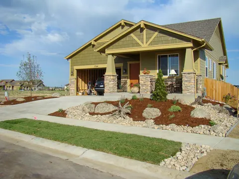 New craftsman style home with fresh mulch, boulders and river rock edging beside the lawn.