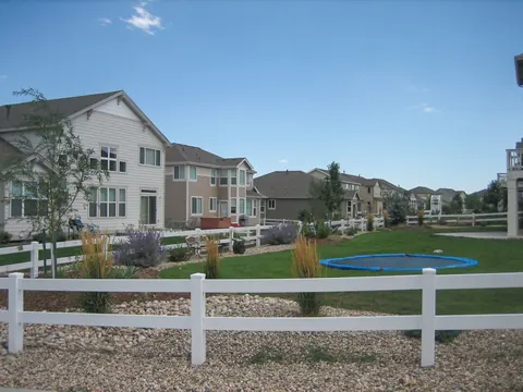 White vinyl fence along a lawn with a river rock border and neighborhood homes beyond.