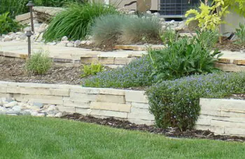 Terraced stacked flagstone retaining walls with blue grasses, perennials and a landscape light.