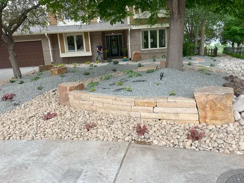 Low stacked flagstone wall in a shaded gravel and river rock front yard in Fort Collins.